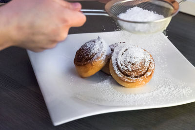 Cropped image of hand sprinkling icing sugar on cinnamon rolls at table
