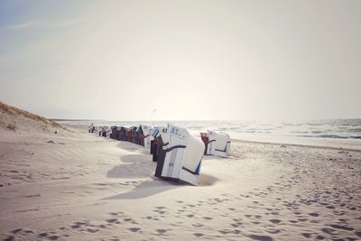 Hooded beach chairs on shore at beach against sky