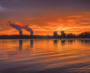 Smoke emitting from factory against sky at sunset