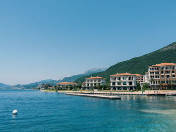 Buildings by sea against clear blue sky