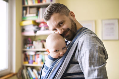 Portrait of smiling father with baby son in sling at home