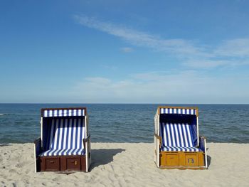 Deck chairs on beach against sky