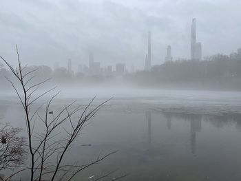 Lake in city against sky during foggy weather