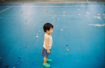 Side view of baby boy standing on old sports court