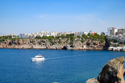 Sailboats in sea by buildings against blue sky