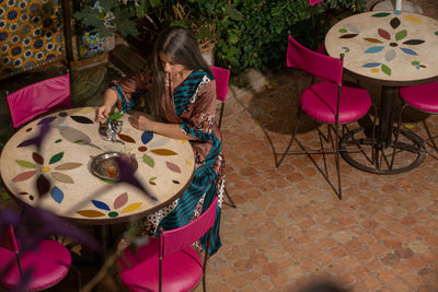 High angle view of woman holding drink in glass while sitting by plants