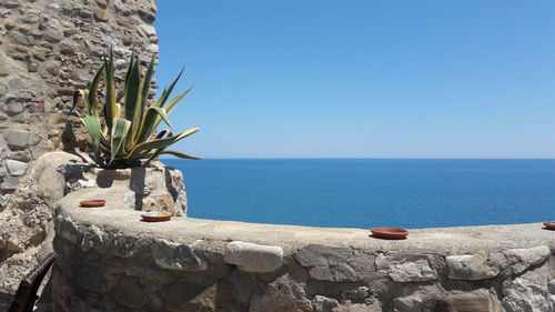 Scenic view of rocks by sea against clear blue sky