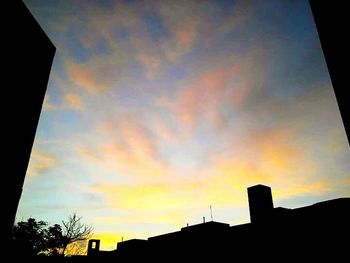 Low angle view of silhouette buildings against cloudy sky