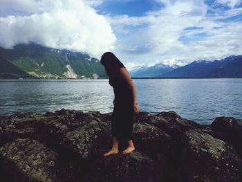 Woman walking on rock at beach against cloudy sky