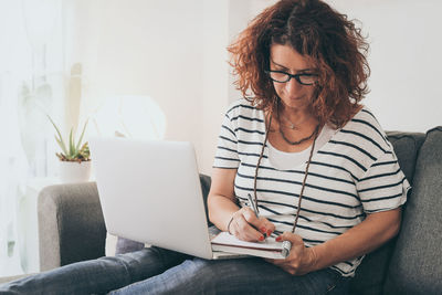 Woman using mobile phone while sitting on sofa at home