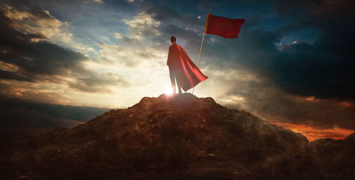 Man in costume standing by flag on mountain against sky at dusk