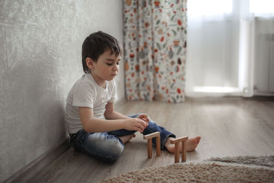 Boy caucasian brunette sad and serious plays on the floor, builds towers from wooden designer, 