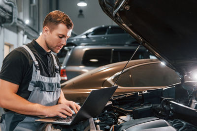 Side view. man in uniform is working in the auto service.