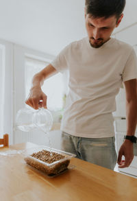 A young man waters wheat seeds into a container.