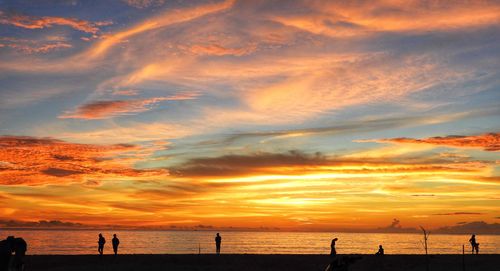 Silhouette people on beach against sky during sunset