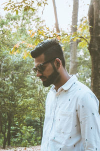 Bearded man standing against trees in forest