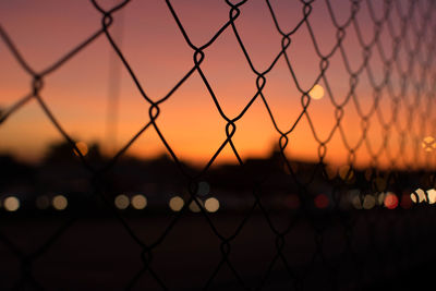 Close-up of chainlink fence against sky during sunset