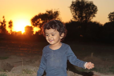 Cute girl standing on field against sky during sunset