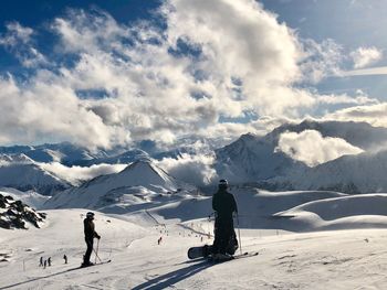 People skiing on snowcapped mountain against cloudy sky