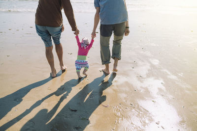 Back view of baby girl walking on the beach with father and grandfather