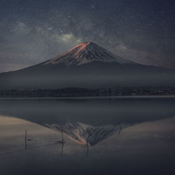 Scenic view of lake by snowcapped mountains against sky at night