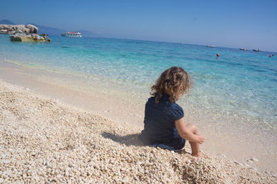 Rear view of girl sitting on sea shore at beach