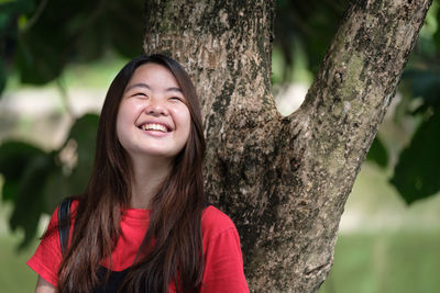 Portrait of a smiling young woman against tree trunk