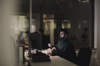 Mid adult businessman having food while working late in office at night