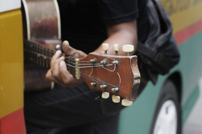 Midsection of man playing guitar while standing against bus