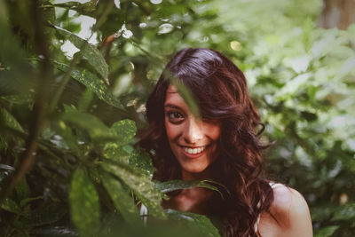 Portrait of smiling young woman standing amidst plants in park