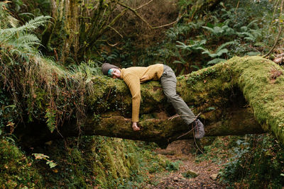 Side view of female explorer lying on tree trunk and having break during trekking in mossy forest