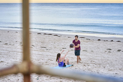 Friends exercising with medicine ball on sand at beach