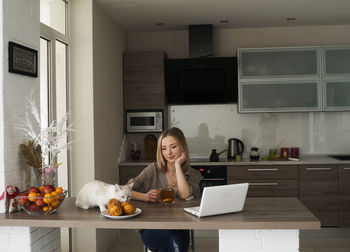 Woman using laptop on table with cat