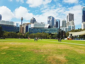 People playing soccer in park against buildings in city against sky