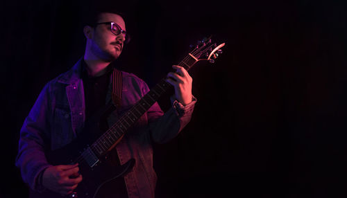 Young adult plays electric guitar under colored lights