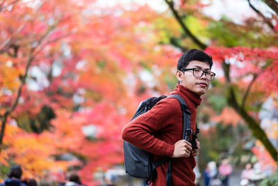 Portrait of young man standing against autumn leaves