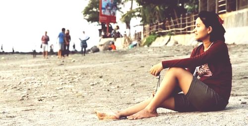 Young woman looking away while sitting on land