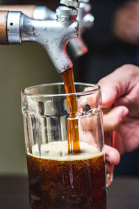 Close-up of cropped hands pouring beer in glass from tap