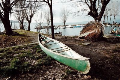 Boat moored by bare trees against sky