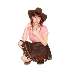 Portrait of woman in dirndl and hat crouching against white background