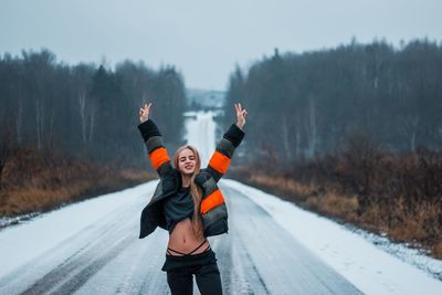 Portrait of woman gesturing peace sign while standing on snowy road