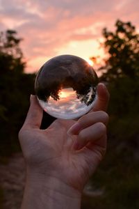 Cropped man holding crystal ball against cloudy sky during sunset