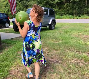 Rear view of senior woman walking while holding watermelon at yard