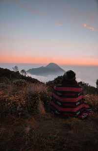 Rear view of woman sitting on land against sky during sunset