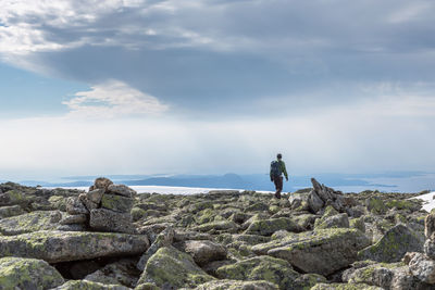 Rear view of hiker on rocks at mountain peak against sky