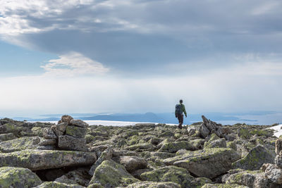 Man standing on cliff by sea against sky