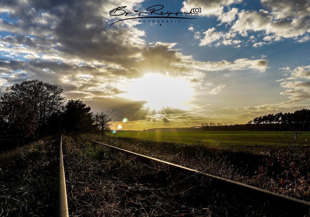 RAILROAD TRACK AMIDST FIELD AGAINST SKY AT SUNSET