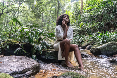 Woman sitting on rock against trees in forest