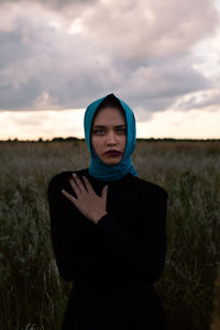 Portrait of young woman standing on field against sky