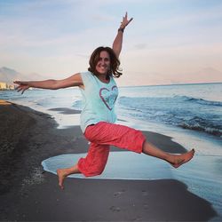 Portrait of smiling young woman jumping on beach against sky